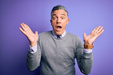 Orta yaşlı, yakışıklı, gri saçlı, mor arka planda zarif bir süveter giyen çılgın ve başarıyı kollarını kaldırıp heyecanla haykıran bir adam. Kazanan konsept