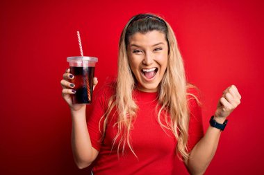 Genç, güzel, sarışın bir kadın kırmızı arka planda saman kullanarak kola içiyor. Gururla bağırıyor, zaferi ve başarıyı kutluyor. Çok heyecanlı, coşkulu bir duygu.