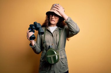 Gezgin şapkası ve su kantini takan güzel bir turist kadın. Dürbünle kafa kafaya dürbün kullanıyor. Utanç ve şaşkınlık dolu bir yüz ifadesi var. Hata için korku ve üzüntü.