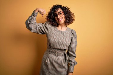 Güzel bir Arap iş kadını. Elbise ve gözlük takıyor. Sarı arka planda duruyor.