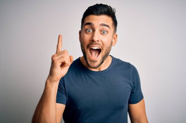Sıradan tişörtler giyen genç yakışıklı adam izole edilmiş beyaz arka planda durup başarılı bir fikir işaret ediyor. Heyecanlı ve mutlu. Bir numara..
