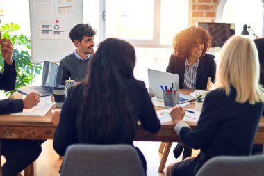 Bir grup iş adamı mutlu ve kendinden emin gülümsüyor. Yüzünde gülümsemeyle çalışmak, dizüstü bilgisayar kullanmak ve ofiste konuşmak.