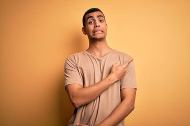 Sarı arka planda dikilen sıradan tişörtler giyen genç ve yakışıklı Afro-Amerikan erkeği endişeli, endişeli ve şaşırmış yüz ifadesini bir kenara bırakıyor.