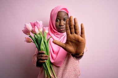 Genç Afro-Amerikan artı boy kadın elinde pembe lale buketi olan Müslüman başörtüsü ile avucunda şarkı söylemeyi kesiyor. Yüzünde olumsuz ve ciddi bir jest olan uyarı ifadesi.