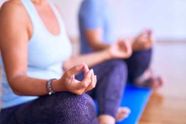 Orta yaşlı, güzel, sportif bir çift mindere oturmuş, yoga yapıyor, spor salonunda nilüfer pozu veriyor.