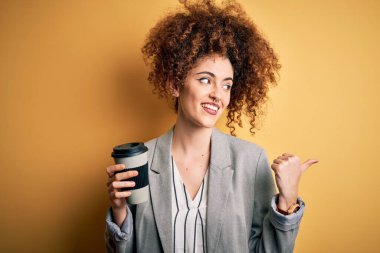 Kıvırcık saçlı ve delici bir bardak kahve içen genç ve güzel bir kadın. Gülümseyen bir gülümsemeyle baş parmağıyla işaret ediyor.