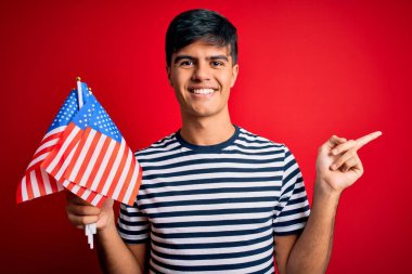 Amerika Birleşik Devletleri bayraklarını tutan genç yakışıklı vatansever adam bağımsızlık gününü kutluyor. Elleri ve parmakları kenarda mutlu mesut işaret ediyor.