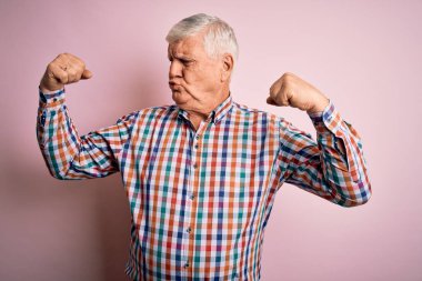 Üst düzey yakışıklı beyaz adam, izole edilmiş pembe arka planda sıradan bir gömlek giyip gururla gülümseyen kol kaslarını gösteriyor. Fitness konsepti.