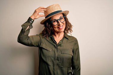 Gözlüklü ve şapkalı orta yaşlı esmer kadın izole edilmiş beyaz arka planda duruyor. Soruları merak ediyor. Şüpheyle kararsız, kafa kafaya düşünerek. Düşünceli kavram.