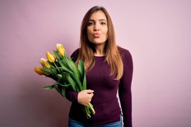 Sarı lale çiçekleri ile dolu romantik bir buketi pembe arka planda tutan genç sarışın kadın havayı öperken kameraya bakıyor. Güzel ve seksi. Aşk ifadesi.