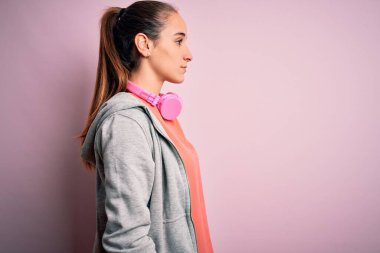 Spor yapan güzel bir kadın müzik dinliyor pembe arka planda kulaklık takıyor, yan yana bakıyor, rahat profil pozu veriyor, kendine güvenen bir gülümsemesi var..