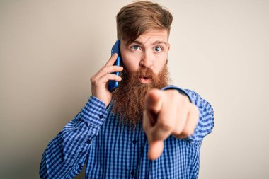 Kızıl saçlı, sakallı İrlandalı bir adam akıllı telefondan konuşuyor izole bir zemin üzerinde kamerayı işaret ediyor ve sen, el işareti, ön taraftan pozitif ve kendinden emin bir jest.