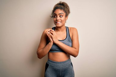 Genç Afrikalı Amerikalı spor kadın spor yapıyor. Beyaz arka planda spor kıyafetleri giyiyor. Gergin ve heyecanlı bir şekilde çene kenarına bakıyor.