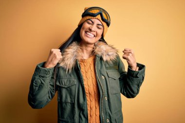 Kış havası için kayak gözlüğü ve palto takan genç ve güzel bir İspanyol kadın kolları havada, gülümseyerek ve başarı çığlıkları atarak çok mutlu ve heyecanlı bir jest yapıyor. Kutlama konsepti.