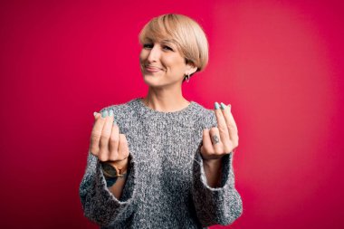 Modern kısa saçlı genç bir kadın pembe arka planda günlük süveter giyiyor. Elleriyle para hareketi yapıyor. Maaş ödemesi istiyor.