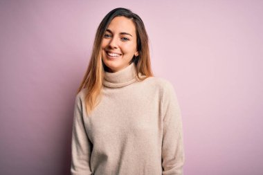 Mavi gözlü güzel sarışın kadın pembe arka planda balıkçı yaka kazak giyiyor ve yüzünde mutlu ve havalı bir gülümseme var. Şanslı kişi..