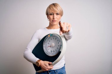 Kısa saçlı, sağlıklı kilosu ve yaşam tarzı için tartısı olan genç sarışın kadın kamerayı işaret ediyor ve sen, el işareti, ön taraftan pozitif ve kendinden emin bir jest.