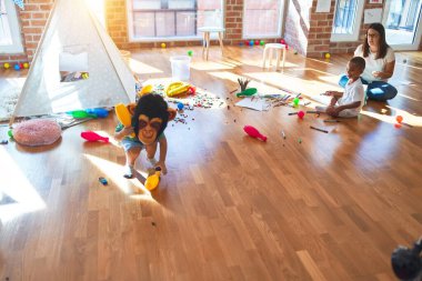 Anaokulunda bir sürü oyuncakla oynayan genç ve güzel öğretmen ve çocuklar.