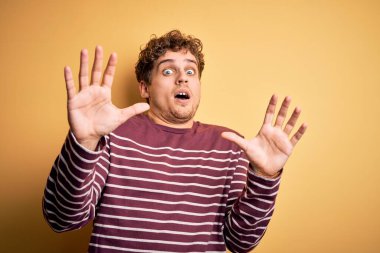 Kıvırcık saçlı, sıradan çizgili süveter giyen, korku ifadesinden korkan genç, sarışın yakışıklı adam. El hareketlerini bırak, şok içinde bağır. Panik konsepti.