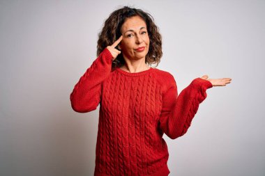 Orta yaşlı esmer kadın, izole edilmiş beyaz arka planda dikilen günlük süveter giyiyor. Avuç içinin açık olması, fotokopi alanını göstermesi ve alnını işaret etmesi kafasını karıştırıyor ve rahatsız ediyor. Bunu bir düşün..