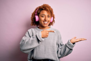 Kıvırcık saçlı, pembe kulaklık takan ve kameraya hayret içinde gülümseyen genç Afrikalı Afro-Amerikalı kadın..