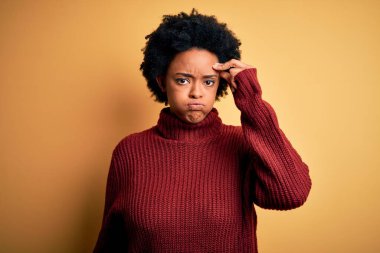 Kıvırcık saçlı, balıkçı yaka kazaklı, alnındaki sorun yüzünden endişeli ve stresli genç Afro-Amerikan kadın.