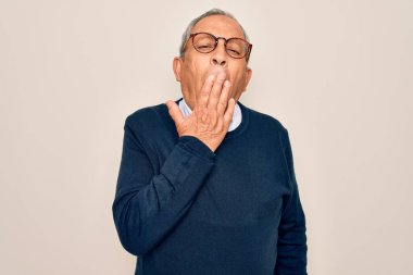 Üst düzey, gri saçlı, süveter giyen ve gözlüklü, izole edilmiş beyaz arka planda esnemekten sıkılmış, ağzı eliyle kapatmaktan bıkmış bir adam. Huzursuz ve uykulu..