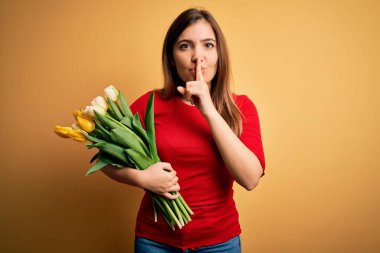 Sarı arka planda romantik lale çiçekleri tutan genç sarışın kadın sessiz olmak istiyor. Sessizlik ve gizli konsept.