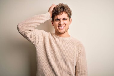 Sarışın, kıvırcık saçlı, beyaz arka planda rahat süveter giyen genç ve yakışıklı bir adam soru sormayı merak ediyor. Şüpheyle kararsız, kafa kafaya düşünerek. Düşünceli kavram.