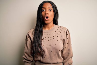 Genç Afro-Amerikan moda kadını kahverengi izole bir arka planda korku, korku ve heyecan dolu bir yüz ifadesinden korkarak ve şok olarak dikiliyor..