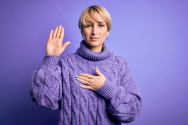 Sarışın, kısa saçlı, balıkçı yaka kazak giyen, mor arka planda elleri göğsünde ve avuçlarında küfreden, sadakat yemini eden genç bir kadın.