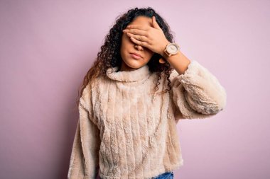 Kıvırcık saçlı genç bir kadın pembe arka planda dikilmiş ciddi ve üzgün görünüyor. Görme, saklama ve reddetme konsepti