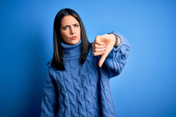 Young brunette woman with blue eyes wearing casual turtleneck sweater looking unhappy and angry showing rejection and negative with thumbs down gesture. Bad expression.
