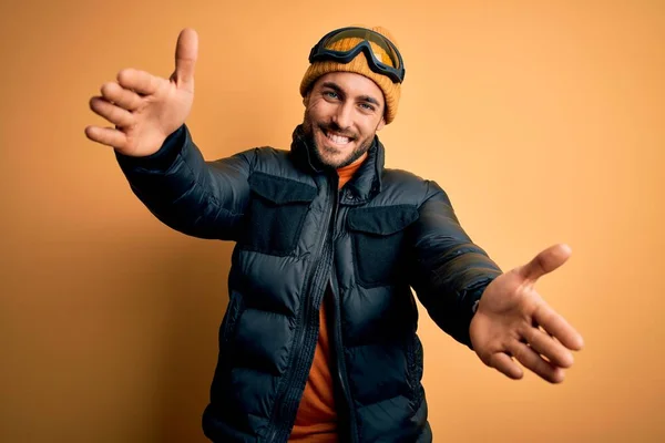 年轻英俊的滑雪者 留着胡子 身穿雪地运动服和滑雪护目镜 看着镜头 张开双臂拥抱 喜庆的表情拥抱幸福 — 图库照片