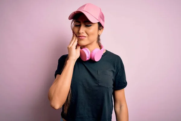 年轻而漂亮的健身女子 戴着训练帽 戴着耳机 戴着粉色背景的训练帽 手牵着嘴 因为牙齿疼痛或牙病 脸上带着痛苦的表情 牙科医生 — 图库照片