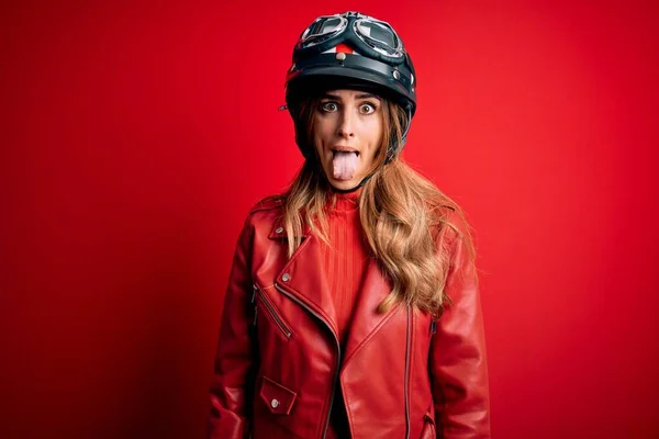 若い美しいブルネットのオートバイの女性は面白い表情で幸せ舌を突き出す赤い背景の上に元ヘルメットを身に着けています 感情概念 — ストック写真