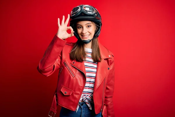 若い美しいブルネットのオートバイのヘルメットと赤いジャケットを身に着けているオートバイの女性は手と指でOkサインをして肯定的な笑みを浮かべている 成功した表現 — ストック写真
