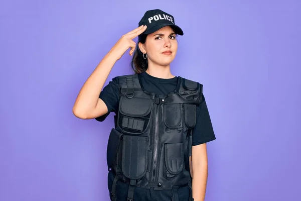 Young police woman wearing security bulletproof vest uniform over purple background Shooting and killing oneself pointing hand and fingers to head like gun, suicide gesture.