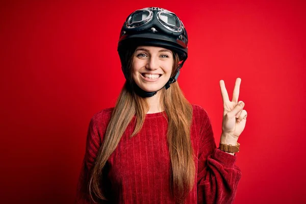 赤い背景に元ヘルメットを被った若い美人の赤毛の元サイクリストの女性が カメラの前で勝利サインをする幸せそうな顔をして微笑んでいる 第二番 — ストック写真