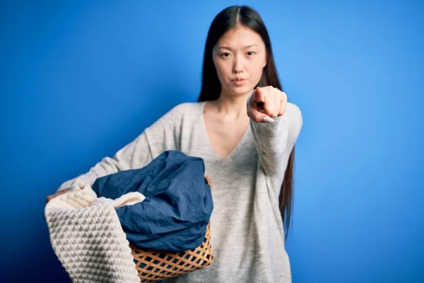 カメラとあなたに指で指差す家事をする邪悪な洗濯バスケットを持っている若いアジアの女性 手のサイン 正とフロントから自信を持ってジェスチャー — ストック写真