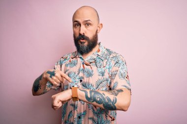 Sakallı ve dövmeli yakışıklı, pembe arka planda sıradan bir çiçek gömleği giyen yakışıklı adam. Aceleyle saati, sabırsızlığı, geç kaldığı için kızgın ve sinirli olduğunu gösteriyor.