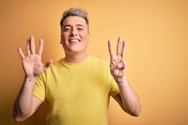 Sarı arka plan üzerinde sarı tişört giyen genç ve modern bir adam 8 numaralı parmaklarıyla gülümseyerek kendinden emin ve mutlu bir şekilde onu işaret ediyor..