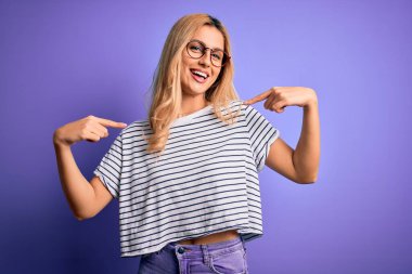 Genç, sarışın, çizgili t-shirt ve gözlük takan, mor arka planda kendine güvenen, gülümseyen, kendini gururlu ve mutlu gösteren bir kadın..