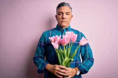 Orta yaşlı, kır saçlı, elinde pembe lalelerle dolu bir buket tutan bir adam.