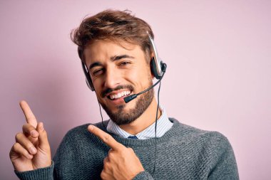 Gizli pembe arka planda sakallı genç bir çağrı merkezi ajanı gülümsüyor ve iki eliyle ve parmaklarıyla kameraya bakıyor..