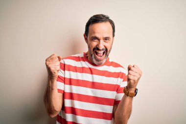 Sıradan çizgili tişört giyen orta yaşlı, beyaz arka planda dikilmiş, kollarını kaldırarak ve açık gözlerle başarının şaşkınlığını ve şaşkınlığını kutlayan beyaz bir adam. Kazanan konsept.