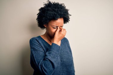 Young beautiful African American afro woman with curly hair wearing casual sweater tired rubbing nose and eyes feeling fatigue and headache. Stress and frustration concept.