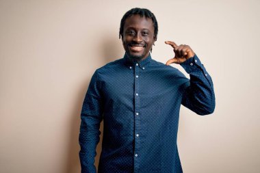 Beyaz arka plan üzerinde dikilen, gülümseyen ve el hareketleriyle küçük boy işareti yapan, parmaklarıyla kameraya bakan Afro-Amerikan genç adam. Ölçü kavramı.
