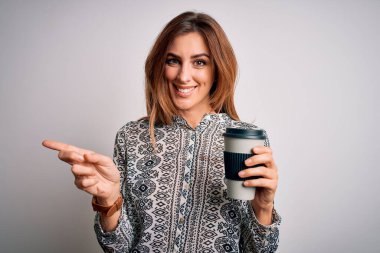Genç, güzel esmer kadın beyaz arka planda bir bardak kahve içerken mutlu bir şekilde elini ve parmağını kenarı işaret ediyor.