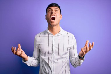 Zarif iş gömleği giyen genç yakışıklı İspanyol adam mor arka planda deli deli deli bağırıyor ve agresif bir ifade ve kollarla bağırıyor. Hayal kırıklığı konsepti.